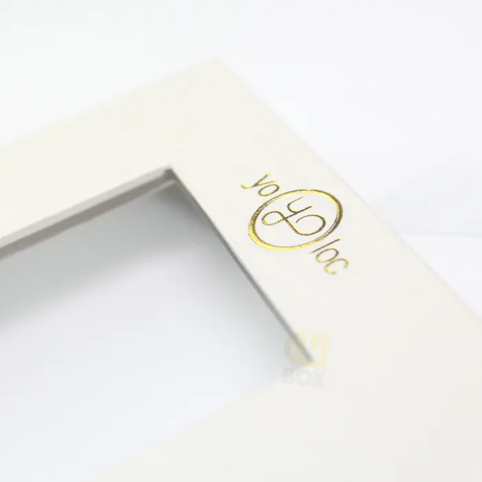 Slanted close-up of metallic gold hot foil logo on luxury white magnetic window gift box packaging