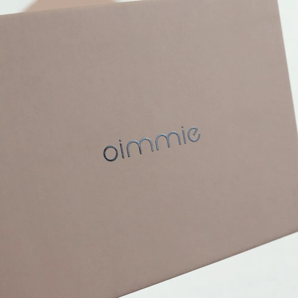 Extreme close-up of debossed silver letter logo detail on soft nude matte perfume box exterior surface