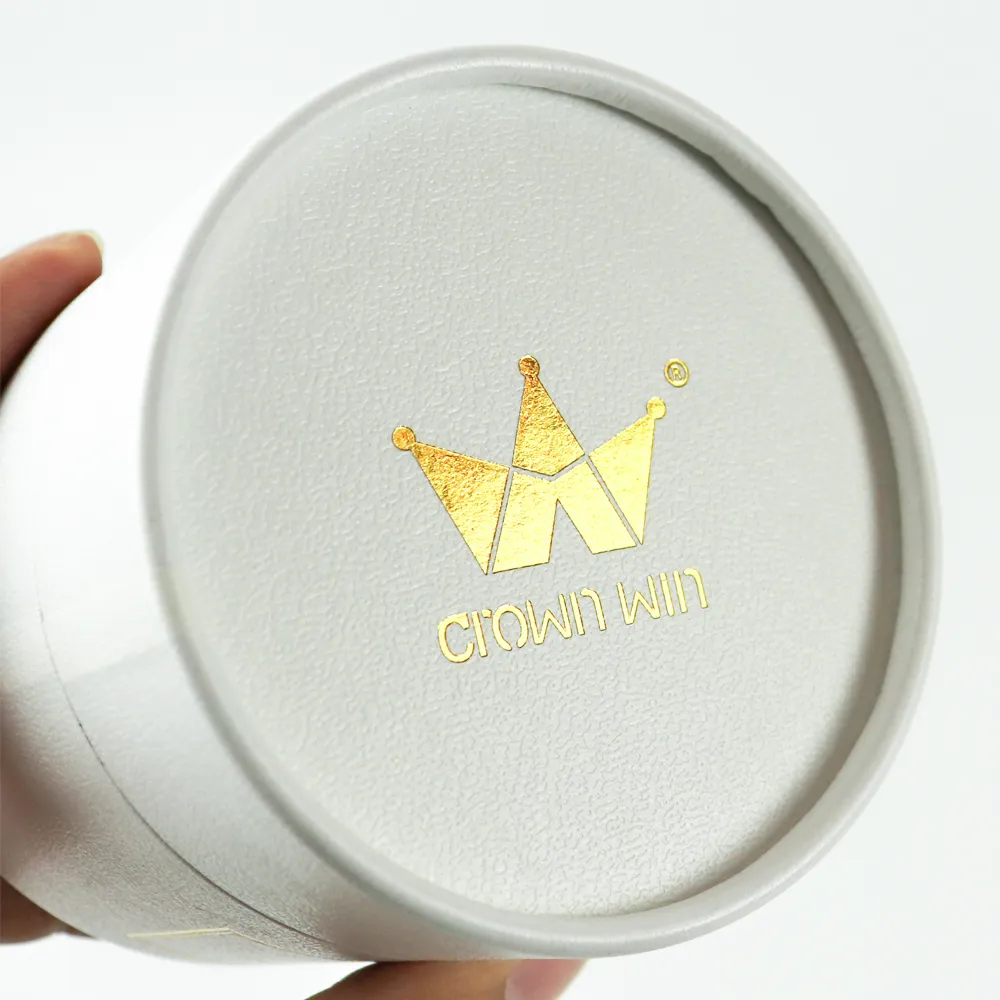 Macro close-up shiny gold foil crown brand logo on textured leather grain round tube lid inside luxury candle boxes