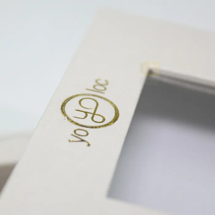 Close-up of custom gold foil stamped brand logo on textured white magnetic rigid window box packaging