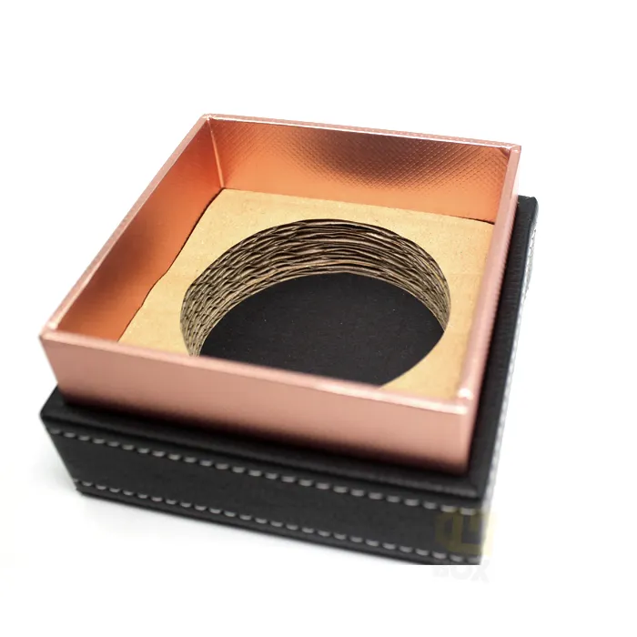 Closed tall rigid candle boxes wrapped in black faux leather grain with white stitching, front panel printed with custom copper hot foil framed brand logo