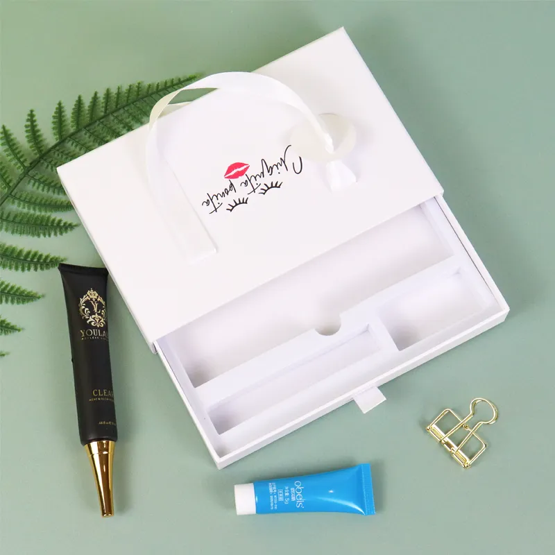 Styled flat lay of white cosmetic boxes with matching skincare tubes, gold binder clip and green fern foliage display
