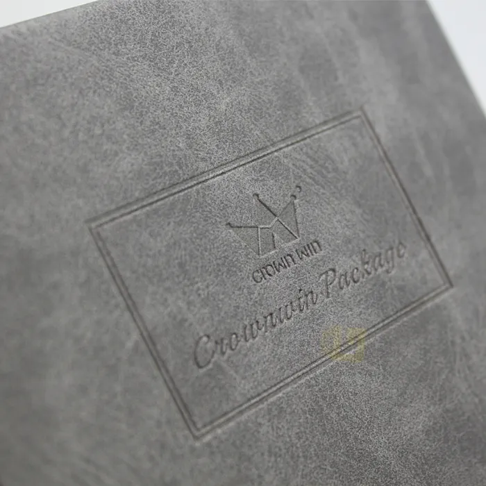 Extreme macro close-up of blind deboss embossed crown logo and brand text on soft grey suede grain candle box exterior