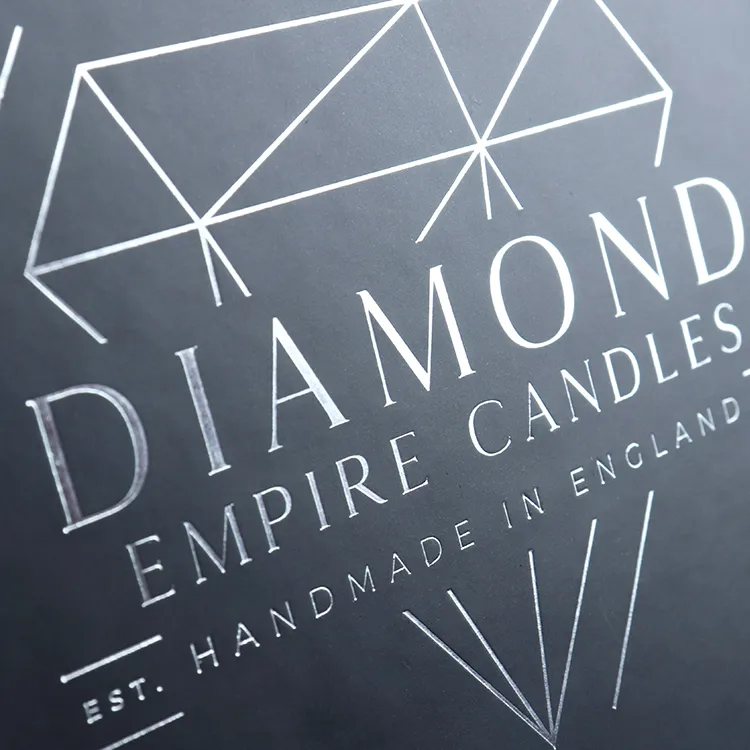 Macro close-up of shiny silver hot foil stamped diamond geometric logo on matte black surface of rigid essential oils boxes, custom print craft detail