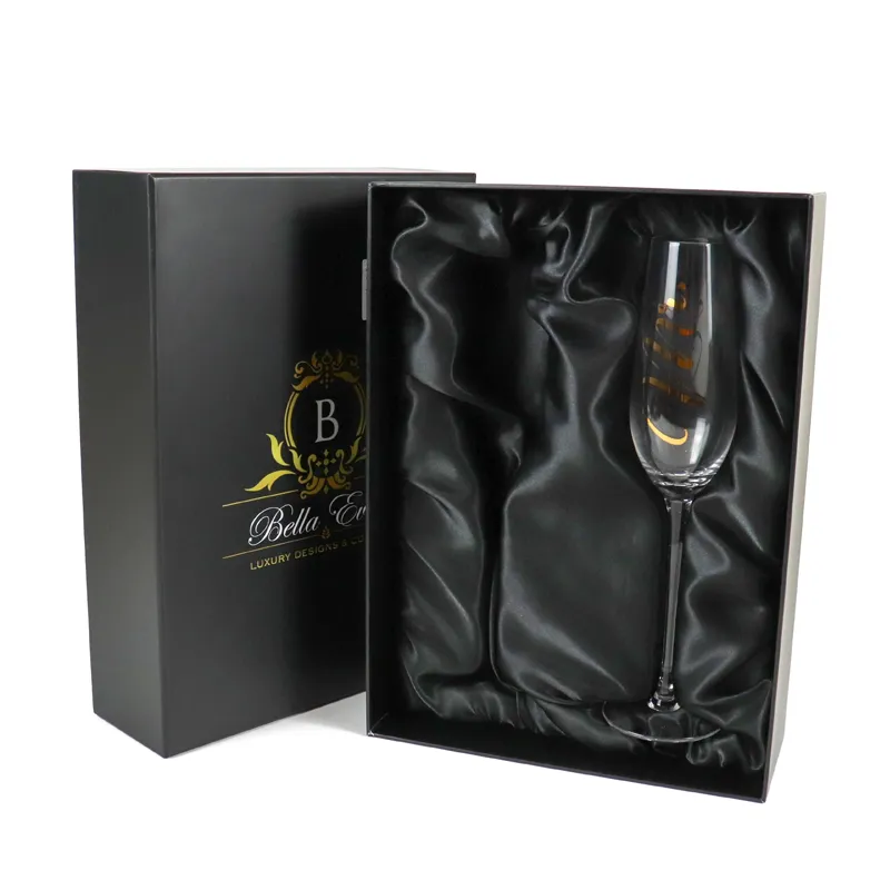 Opened matte black lid and base rigid gift box with draped black satin lining and engraved champagne flute inside