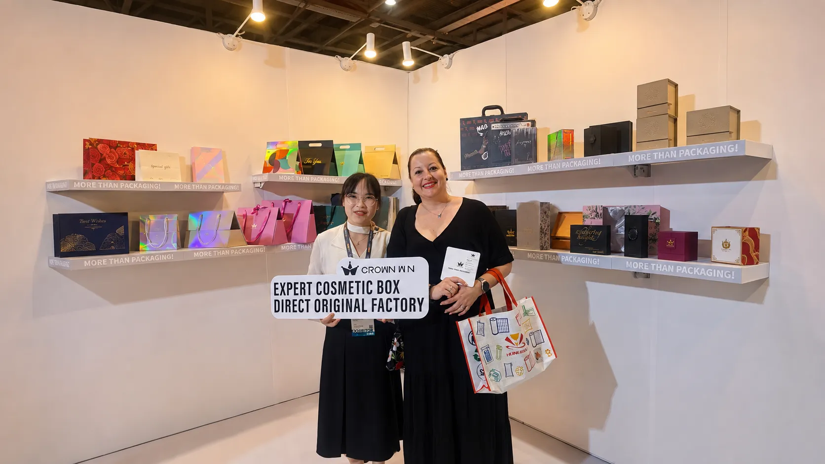 Crown Win sales representative and overseas female buyer pose for photo in front of gift box & paper bag display wall at Hong Kong fair