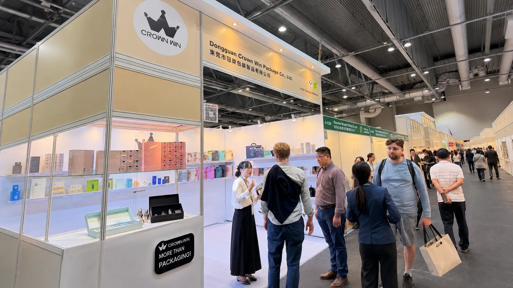 Full overview of Crown Win booth at Hong Kong packaging fair, sales team introducing luxury paper packaging samples to trade visitors